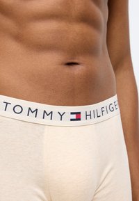 Μπεζ βαμβακερές boxers με μαλακή ελαστική ζώνη που φέρει το λογότυπο "TOMMY HILFIGER" σε σκούρο μπλε, κόκκινο και λευκό χρώμα. Απαλή υφή.