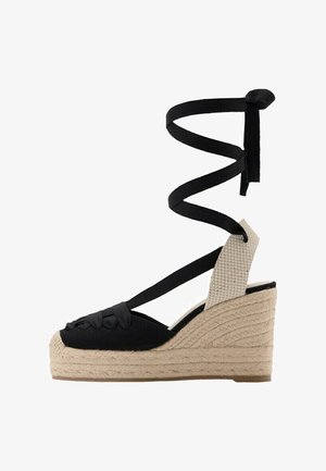 Schwarze Espadrilles-Sandale mit Keilabsatz aus Stoff, beige geflochtener Jute-Plattform und Wickelverschluss um den Knöchel.
