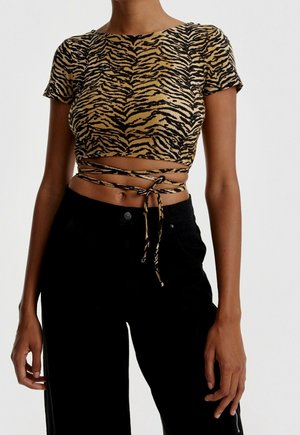 Vrouw die een cropped wikkeltop met tijgerstrepen en korte mouwen draagt, om de taille gestrikt, gecombineerd met een hooggetailleerde zwarte broek.