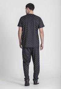 Čierny bavlnený outfit so vzorovanou košeľou s krátkym rukávom a zodpovedajúcimi nohavicami, obidve s geometrickým dizajnom a vo voľnom strihu.