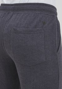 Gray cotton blend joggers featuring a textured material, elastic waistband, and a back pocket with a triangular logo detail.