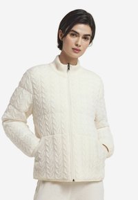 Veste blanche en maille avec col montant, fermeture éclair frontale et motif torsadé texturé, dotée de deux poches latérales. Matière douce et confortable.