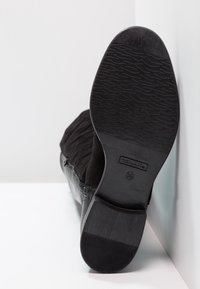 Botín negro hasta el tobillo con un upper de ante texturizado y un acabado mate suave. La suela presenta un grip con patrón y un detalle del logo.