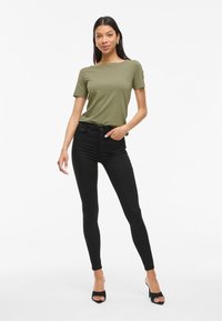 Olivgrön t-shirt med kort ärm, som vi kombinerat med hög midja svarta skinny jeans och svarta klacksandaler. Slät tyg och figurnära design.