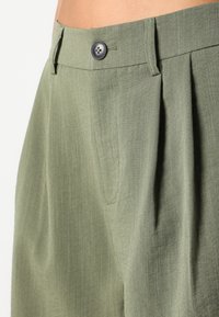 Pantalons plissés verts en tissu léger, dotés d'une fermeture à bouton et d'une texture subtile. Coupe ajustée avec poches latérales.