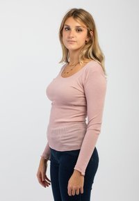 Top a maniche lunghe ribbed rosa chiaro con scollo a barco e polsini sfrangiati, abbinato a jeans scuri. Il tessuto appare morbido e aderente.