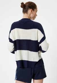 Navy en crèmekleurige gestreepte gebreide trui met een losse pasvorm, brede mouwen en textuurstof. Voorzien van zij-openingen en een geribbelde zoom.