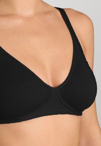 Sostenitore in tessuto nero con design a scollatura a V, texture morbida e coppe senza cuciture. Presenta spalline sottili e una forma classica per supporto.