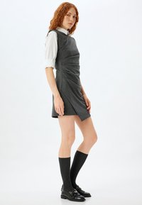 Grijsstens gestreepte jurk met zijdraping, gedragen over een witte coll shirt. Zwarte instappers en donkere kniekousen maken de look af.