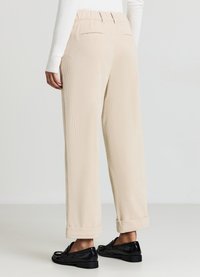 Beige Cordhosen mit lockerem Schnitt, ausgestattet mit flexiblem Bund, umgeschlagenen Beinabschlüssen und zwei Gesäßtaschen. Dazu schwarze Loafers getragen.