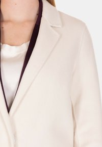 Blazer beige chiaro con colletto a punte, realizzato in tessuto testurizzato. Caratterizzato da una fodera di un profondo viola e chiusura con un solo bottone.