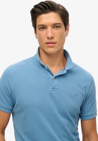 Polo shirt azzurro chiaro realizzato in tessuto testurizzato, con colletto, pattina con due bottoni e logo ricamato sul lato sinistro del petto.