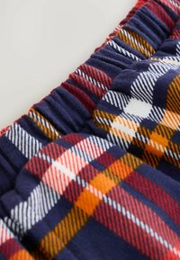 Tissu en tartan bleu marine avec des motifs rouges, jaunes et blancs. Texture douce avec une taille élastique froncée. La vue en gros plan met en avant le motif.