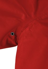 Roter Jackenstoff mit glatter Textur und Rautenmuster. Verfügt über einen schwarzen Metallösen an der Schulternaht für Details.