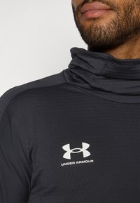 Dark gray athletic top with a high collar, textured fabric, and white Under Armour logo on the chest area.