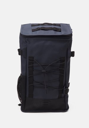 Sac à dos haut bleu marine avec cordon élastique noir à l’avant, poche latérale en mesh, fermeture éclair sur le dessus et sangles d’ajustement latérales noires.