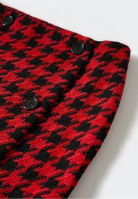 Tela con patrón de pata de gallo en rojo y negro, con cuatro botones negros; tejido texturizado con detalle de diseño destacado.