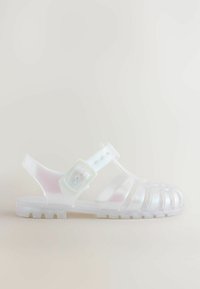 Transparent jelly sandal med ett crisscross remdesign, justerbar ankelslejf och en strukturerad sula för ökat grepp.