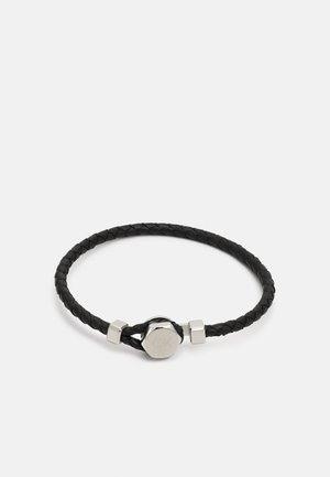 Pulsera de cuero trenzado negro que presenta un cierre metálico con detalle grabado y acentos geométricos, ofreciendo un diseño texturizado y estructurado.