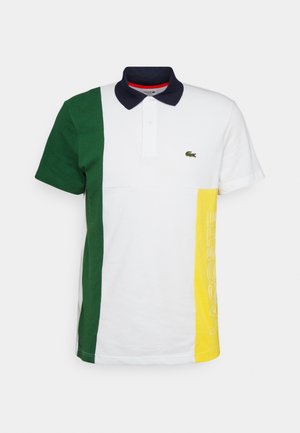 Poloshirt mit dunkelgrüner linker Seite, weißem Mittelteil, gelbem rechtem Seitenteil mit dem Text "LACOSTE", marineblauem Kragen und kleinem Krokodil-Logo auf der Brust.