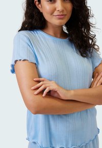 Ljusblå kortärmad topp med ribbat mönster, vågiga kanter och vertikala ränder. Tyget verkar mjukt och något strukturerat.