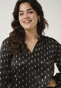 Black blouse with gold leaf patterns, v-neckline, and gathered accent at sleeves. Soft texture with subtle sheen.