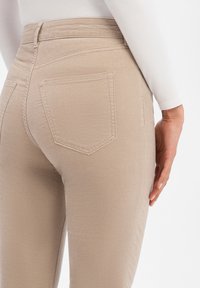 Beige high-waist jeans met een aansluitende pasvorm, achterzakken met dubbele stiksels en een gladde textuur. Gemaakt van een zachte katoenmix.