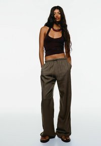 Tmavohnedý crop top s halter krkom; voľné olivovo zelené nohavice s elastickým pásom; nosené s čiernymi sandálmi.