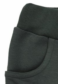 Ciemnozielone spodnie dresowe z prążkowanym paskiem, boczną kieszenią i miękką bawełnianą fakturą. Tkanina jest gładka, z detalami szwów.