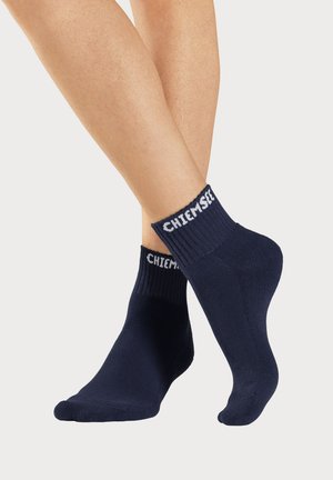 Navy ankle socks made of a smooth fabric, featuring a ribbed cuff and white "Chiemsee" text at the top. Seamless toe design.