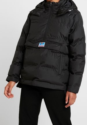 Giubbotto imbottito nero con colletto alto, chiusura zip e una grande tasca frontale. Presenta bottoni a pressione sulle spalle e patch con logo sul petto.