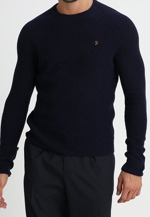 Marineblauwe geribbelde trui met een ronde hals en lange mouwen. Heeft een klein geborduurd logo op de borst en strakke manchetten.