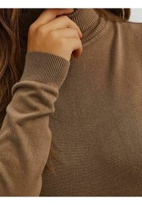 Brauner Rollkragenpullover, gerippte Bündchen und Kragen, weiche Textur, figurbetontes Design, Nahaufnahme des Stoffes und Handposition.