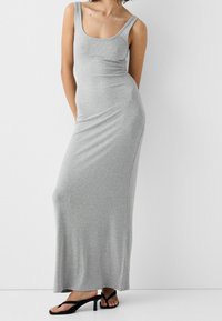 Robe débardeur grise à côtes avec une silhouette ajustée, décolleté en scoop et poches latérales. Associée à des tongs à talons noires.