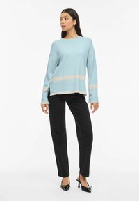 Pull à manches longues bleu clair avec rayures crème, coupe décontractée, fentes latérales, associé à un pantalon noir droit et des chaussures à talons noires.