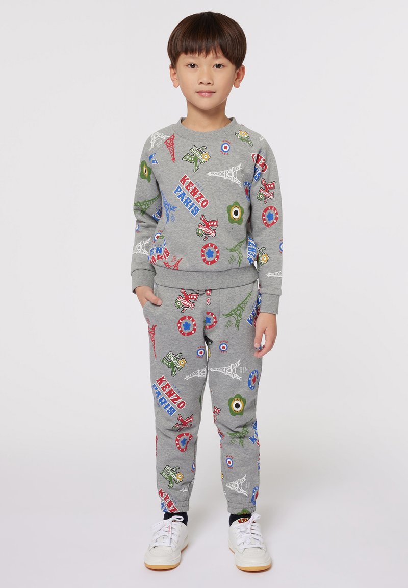 Sweatshirt gris à manches longues et pantalon assorti avec des impressions graphiques colorées, incluant des monuments et des personnages. Tissu en coton, poignets côtelés.