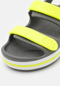 Šedé sandály se dvěma širokými neonově žlutými pásky, texturovanou stélkou a bílou podrážkou s žlutým akcentním pruhom. Obsahují kruhový texturovaný detail.