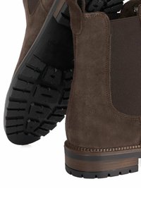Brown suede ankle boot with elastic side panels, textured black rubber sole, and detailed stitching along the base.
