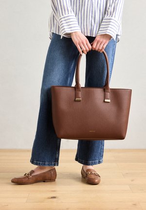 Pruunist nahast kott kahe pealmise käepidemega, ristkülikukujuline ja tekstureeritud pind, millel on minimaalne riistvara ja kuldne brändi logo.