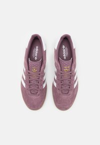Adidas-sneakers i dämpad mauve mocka med vitt tre-stripes-design, texturerad tånbox och guld-logotypdetalj på tungan.