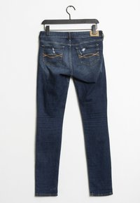 Jeans skinny de denim azul oscuro con una textura suave, que presentan dos bolsillos traseros con costura clara y un ligero desgastado encima de los bolsillos.