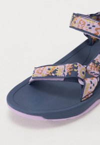 Marine sandal med strukturert gummisåle og flerfargede mønstrede stropper i nyanser av rosa, oransje og blått. Justerbare borrelås.