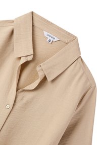 Camicia beige con collare in tessuto strutturato, dotata di chiusura a bottone e un'etichetta che riporta la scritta “Terranova” con le etichette delle taglie visibili.