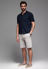 Marineblaues Kurzarmhemd mit Knopfleiste und Kragen, kombiniert mit hellgrauen Shorts. Graue Schuhe ergänzen das Outfit. Glatte Stoffstruktur, lässige Passform.