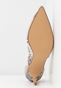 Chaussure à talon haut à bout pointu avec motif imprimé serpent, vue de la semelle sur fond blanc.