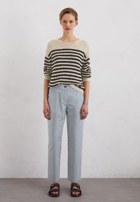 Pull en tricot avec des rayures crème et noires, associé à un pantalon loose bleu clair. Sandales noires avec des accents en métal doré.