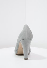 Chaussure à talon haut en daim gris avec un bout pointu et un talon épais, présentant une texture lisse et une semelle intérieure rembourrée visible depuis l'arrière.