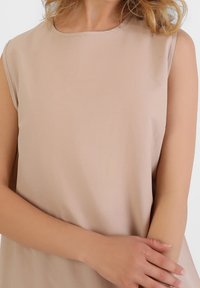 Beige ærmeløs top med rund halsudskæring, lavet af glat stof, med en afslappet pasform og minimale syninger.