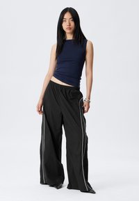 Débardeur sans manches navy associé à un pantalon large noir, avec des passepoils blancs, une taille élastique et une texture de tissu lisse.