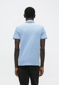 Lichtblauwe polo met een gestructureerde stof, korte mouwen, contrasterende donkere afwerking bij de kraag en mouwranden, gecombineerd met een donkere spijkerbroek.